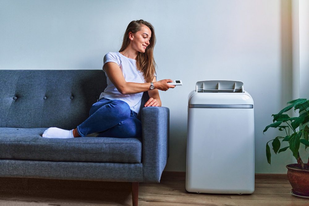 young-casual-woman-sitting-sofa-using-floor-air-conditioner-cooling-hot-summer-weather-fresh-clean-air-home